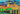 A colorful, stylized cityscape artwork featuring a large cathedral with domes, a stone bridge over water, trees, and swirling patterned clouds in vivid blue, green, yellow, orange, and red tones.
